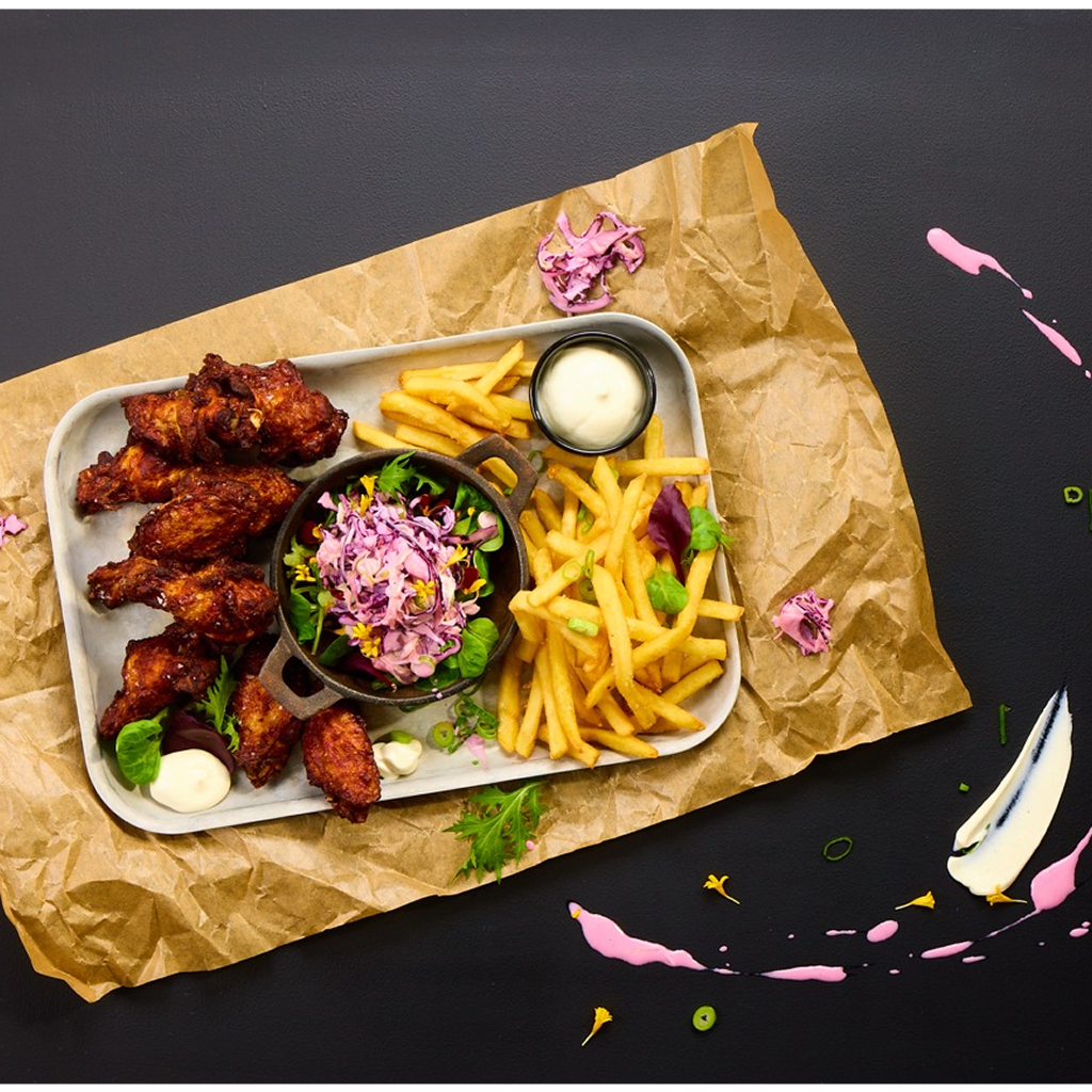 Knusprig frittierte Chicken Wings und goldbraune Pommes Frites auf einem Tray, angerichtet mit Pink Slaw, Frühlingszwiebeln und cremiger Arizona Ranch Sauce als Dip